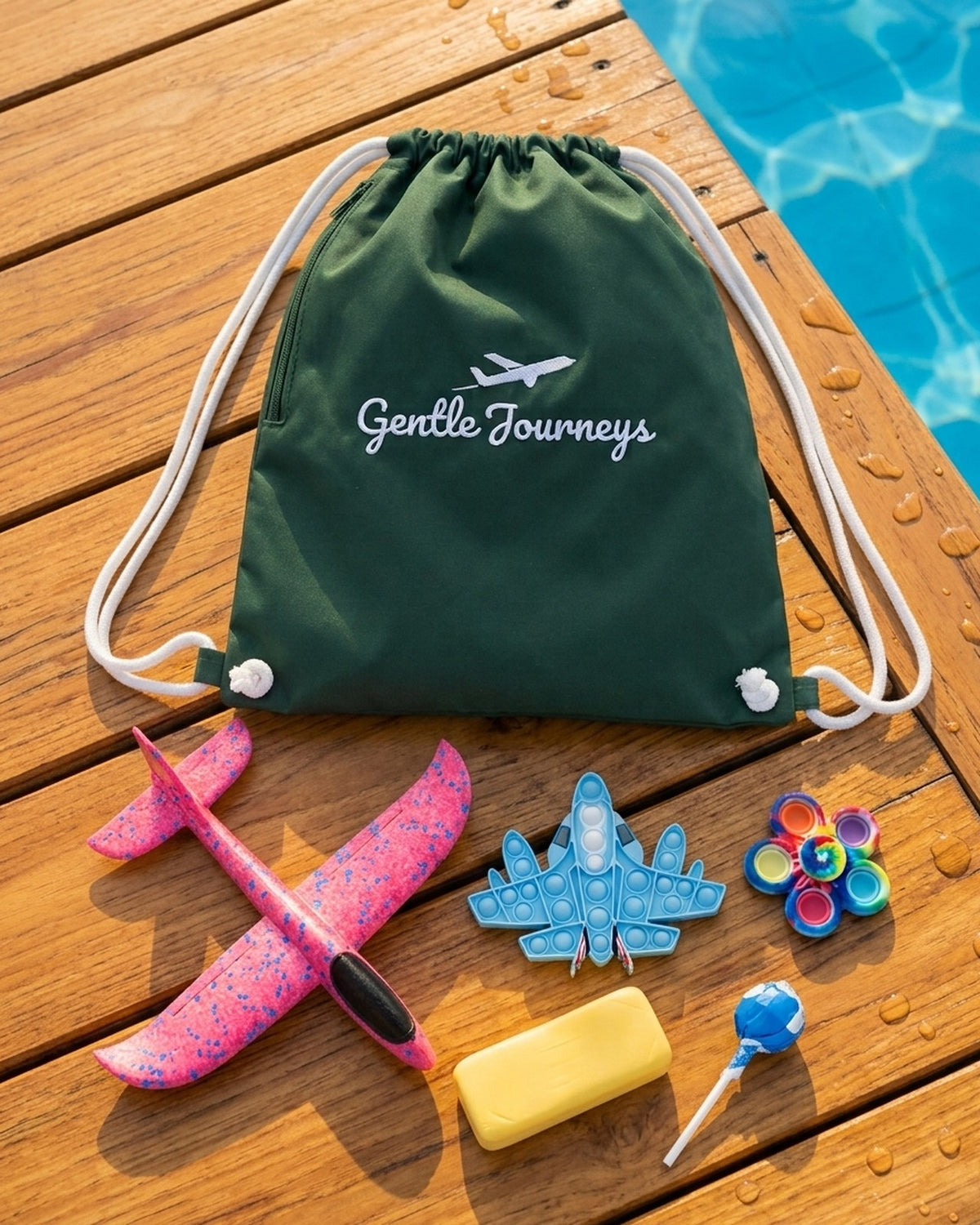 Green Water-Resistant sensory travel bag on wooden poolside decking with the foam glider, aeroplane pop it, tie-dye spinner, butter stress bar and sugar-free lollipop