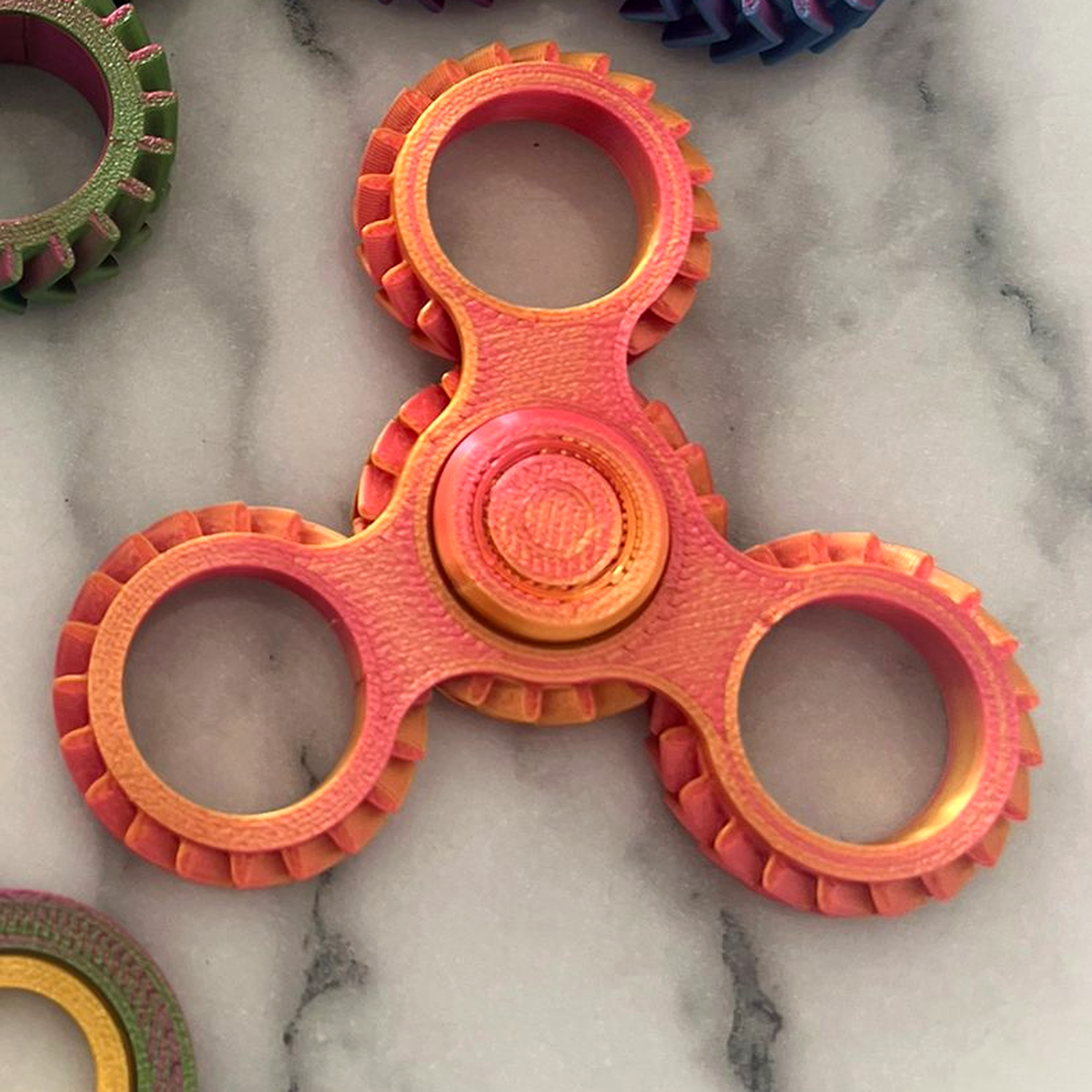 Gentle Journeys fidget spinner, 3D printed in pearlescent orange and pink PLA, on a marble surface